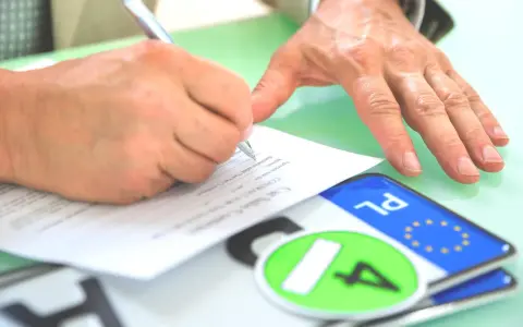 Podpisanie umowy kupna-sprzedaży pojazdu, co jest kluczowe dla uzyskania homologacji. Obok dokumentów leżą tablice rejestracyjne.