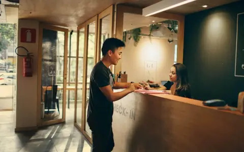 Mężczyzna melduje się w hotelu. Pracownica recepcji wyjaśnia, ile zarabiają turcy w hotelach, gdy obsługuje gościa.