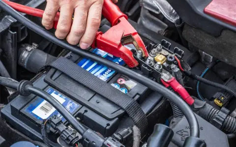 Starthilfe war zuerst: Eine Hand befestigt eine rote Klemme an der Autobatterie, um dem Fahrzeug wieder Leben einzuhauchen.
