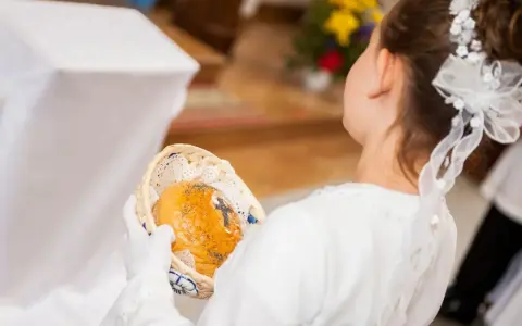 Dziewczynka w bieli trzyma koszyczek z opłatkiem. Zastanawiasz się, ile daje chrzestny na komunię?