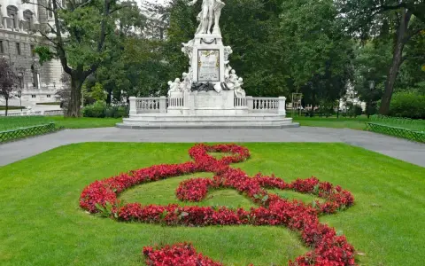 Pomnik Mozarta w Wiedniu, z kluczem wiolinowym ułożonym z czerwonych kwiatów na trawniku.