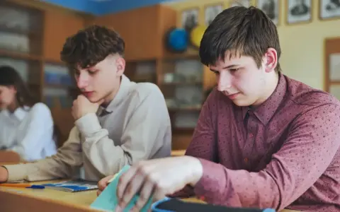 Uczniowie w klasie, jeden z nich zamyślony, inny przegląda notatki. Czyżby czekał na ocenę, która może oznaczać nieklasyfikowanie ucznia?