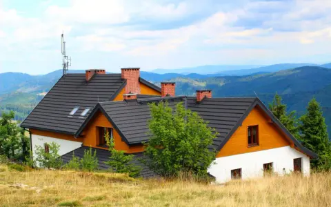 Wielka racza na dachu domu w górach, otoczona zielenią i widokiem na pasma górskie.