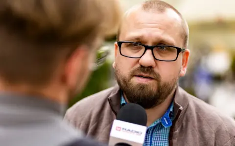 Mężczyzna w okularach udziela wywiadu mikrofonowi radiowemu.