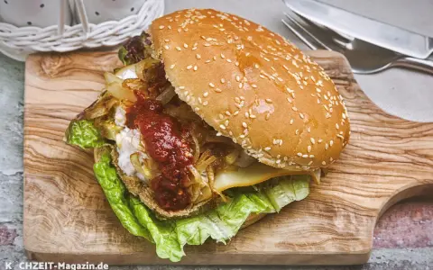 Ein saftiger vegetarischer Burger mit Salat, karamellisierten Zwiebeln und scharfer Sauce auf einem Holzbrett.