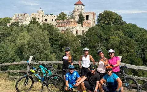 Grupa rowerzystów na tle ruin zamku. Planują noclegi na Szlaku Orlich Gniazd rowerem.