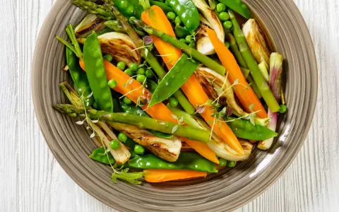 Jardinière de légumes colorée : carottes, pois, asperges et fenouil grillés, garnie de thym frais. Un plat sain et appétissant.