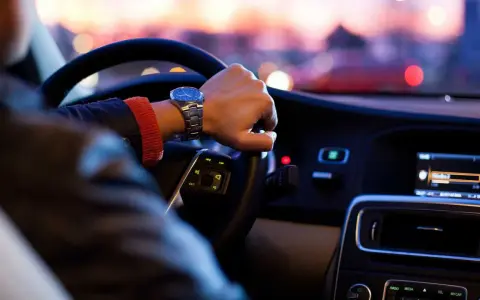 Kierowca w samochodzie ciężarowym do 3,5 tony sprawdza kilometrówkę na zegarku, jadąc nocą przez miasto.