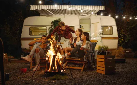 Freunde genießen einen gemütlichen Abend bei Lagerfeuer und Gitarrenmusik während ihres Campingurlaubs in Deutschland.