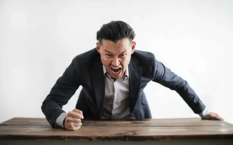 Wütender Mann im Anzug schreit über einen Tisch. Darf ein Lehrer Schüler anschreien?
