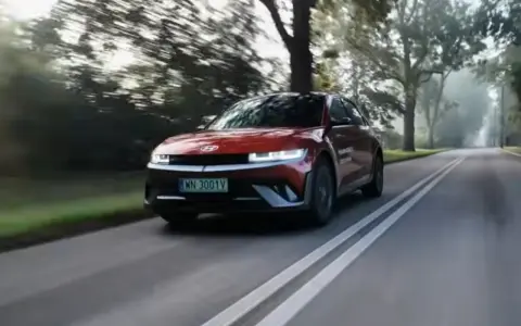 Czerwony Hyundai Ioniq 5 jedzie po wiejskiej drodze wśród drzew.