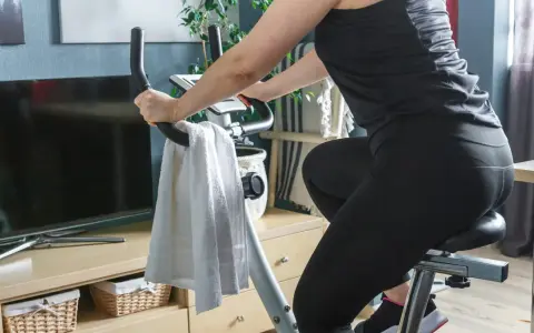 Kobieta w czarnym stroju ćwiczy na rowerze stacjonarnym, spędzając godzinę jazdy na rowerze stacjonarnym w domowym zaciszu.
