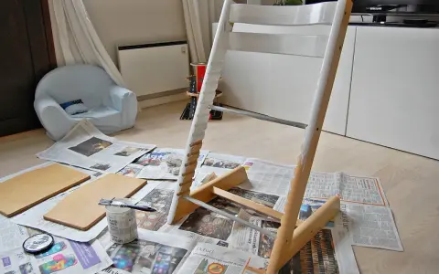 Måla om Stokke stol med vit färg. Trädelar och pensel ligger på tidningspapper.
