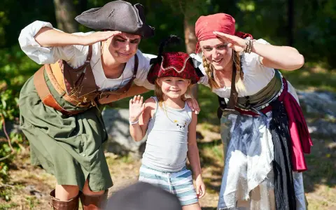 Två pirater och ett barn ler och hälsar. En rolig dag med aktiviteter för barn.