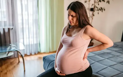 Schwangere Frau im 3. Trimester mit oberbauchschmerzen, hält sich den Rücken.