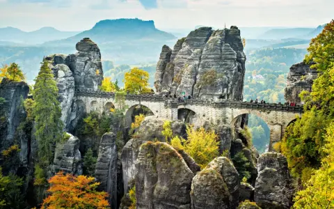 Most Bastei, skalne miasto w Saksonii, z kamiennym mostem łączącym skalne iglice. Jesienne liście dodają koloru krajobrazowi.