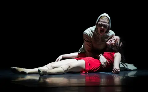 Una escena dramática de "Romeo y Julieta resumen corto": una mujer con capucha grita sobre otra, vestida de rojo, que yace en el suelo.