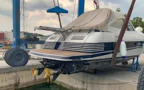 Ein luxuriöses Motorboot wird für das Winterlager aus dem Wasser gehoben. Zwei goldene Propeller ragen aus dem Rumpf.
