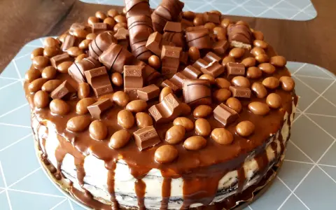 Pyszny tort kinder bueno, obficie udekorowany kawałkami batoników i czekoladowymi drażetkami, spływający karmelem.