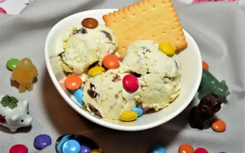 Schüssel mit cremigem Eis, garniert mit bunten Smarties und einem Keks. Kleine Figuren schmücken die Szene.