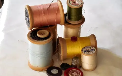 Bobine di filo colorato, bottoni e un ditale, pronti per un punto sopraggitto a mano.
