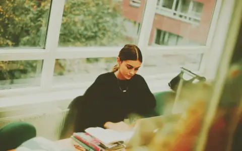 Studentka pochłonięta nauką kryminologii w Poznaniu, siedzi przy oknie z laptopem i książkami.