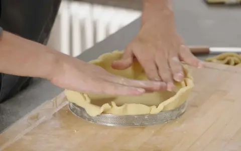Mains expertes pour foncer une pâte dans un cercle à tarte. La pâte est étalée et ajustée sur les bords.