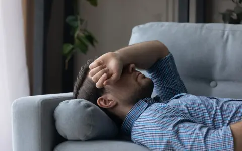Mann liegt erschöpft auf Sofa, Hand vor dem Gesicht. Er sucht nach Tipps, wie man nach Koks schlafen kann, um endlich Ruhe zu finden.
