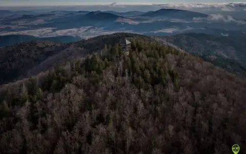 Wieża widokowa na szczycie góry, otoczona lasem. W oddali rozciągają się pasma górskie i doliny. Mogielica szlaki zapraszają do odkrywania piękna Beskidu Wyspowego.