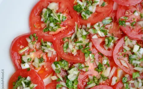 Fette di pomodoro fresco condite con cipolla tritata e erbe aromatiche. Un'insalata di pomodori semplice e gustosa.