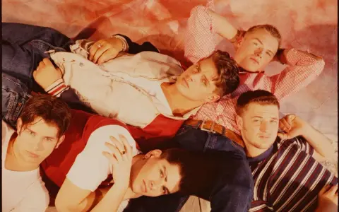 Medlemmar av Boyzone ligger tätt tillsammans, klädda i jeans och färgglada toppar.