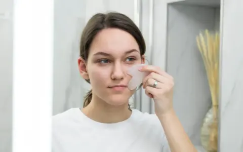 Une jeune femme utilise un gua sha pour un massage facial, un remède de grand-mère pour un visage gonflé.
