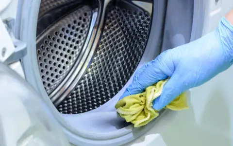 Mano con guante azul limpiando la goma de la lavadora con un paño amarillo. Un método natural para limpiar lavadora vinagre y bicarbonato.