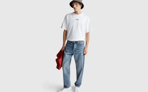 Uomo con t-shirt bianca "LOVE", cappello bucket grigio e jeans relaxed fit. Il significato di questi jeans è comfort e stile casual.
