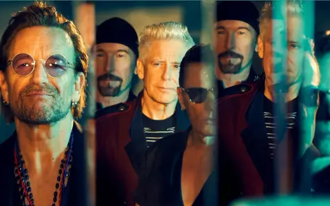 Le groupe U2, avec Bono au premier plan, pose en groupe, leurs visages reflétant une lumière tamisée.
