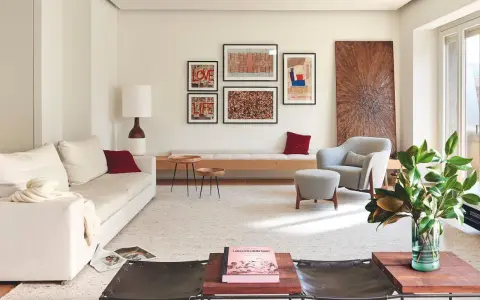 Una composición de cuadros en la pared, con arte abstracto y tipografía, decora este salón moderno junto a un sofá blanco y una butaca gris.