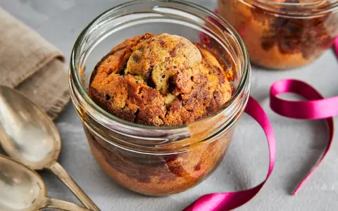 Zwei köstliche Kuchen im Glas, mit Schokoladenstückchen, warten auf Löffel. Eine pinke Schleife und Leinentuch deuten auf ein besonderes Geschenk hin.