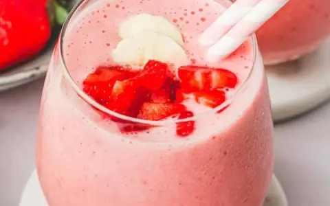 Un délicieux smoothie fraise banane, garni de morceaux de fruits frais et de pailles rayées roses et blanches.