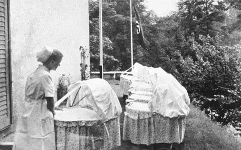 Pielęgniarka przy wózkach dziecięcych. Flaga nazistowska w tle. To obrazek z czasów Lebensborn, co to za program?