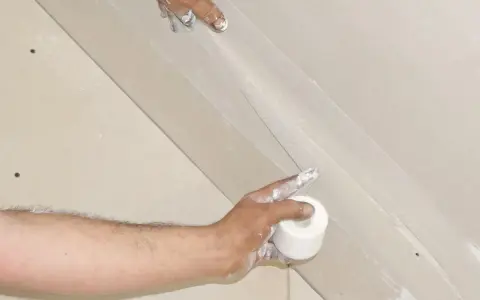 Hände arbeiten an einer q4 Spachtelung. Eine Rolle Klebeband wird gehalten, während die andere Hand die Spachtelmasse aufträgt.
