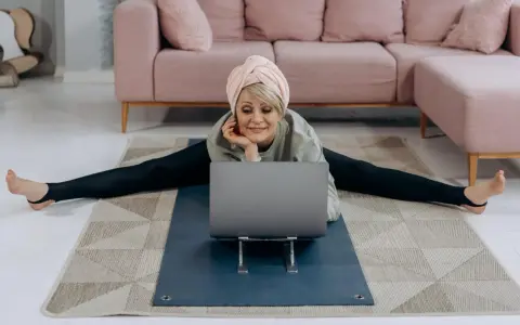 Kvinna i spagat framför laptop, med en rosa soffa i bakgrunden. Hon verkar lära sig om fosfor i kroppen.