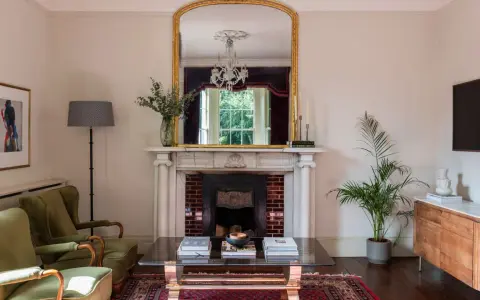 Sofá verde, chimenea con espejo dorado y candelabros. La sala de estar exhibe colores elegantes y un ambiente acogedor.