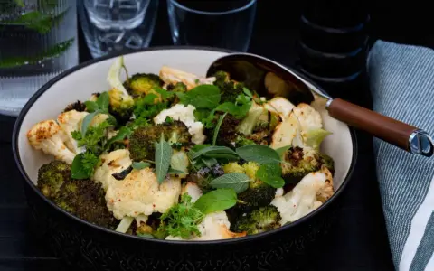 En skål med ugnsrostad blomkål och broccoli, toppad med färska örter. Perfekt som tillbehör till middagen.