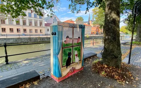 En målad låda med två katter som tittar ut genom ett fönster på ett slott. Konstnären har valt att måla tunt för att ge en drömsk känsla.