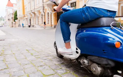 Un uomo in jeans guida uno scooter blu su un lastricato, un'immagine che evoca la libertà e lo spirito dell'art 52 cds.