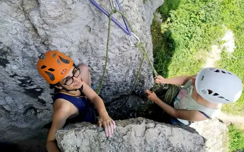 Dwie osoby w kaskach wspinają się po skale na Jurze Krakowsko-Częstochowskiej.