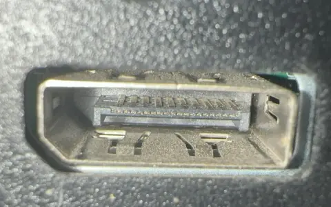 Närbild på ett dammigt displayport uttag med synliga kontakter och fästen.