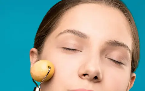 Mujer con ojos cerrados disfrutando de un masaje facial antienvejecimiento y drenaje con rodillo de jade.