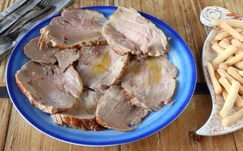 Plato azul con lonchas de jugosa carne mechada, servida con palitos de pan crujientes al lado.