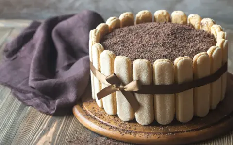 Wykwintny tort tiramisu, otoczony biszkoptami i ozdobiony czekoladową posypką, prezentuje się apetycznie.